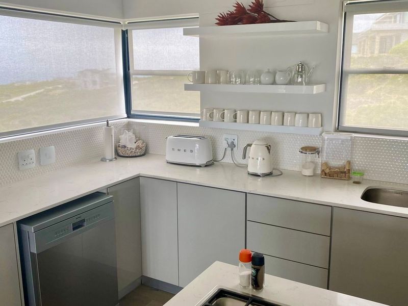 Modern kitchen featuring stone countertops, a gas hob with extractor, integrated dishwasher, and floating shelving with a coastal view.