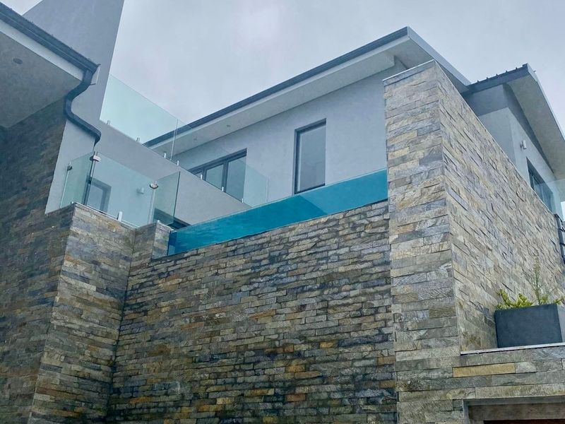 A modern architectural exterior featuring a striking elevated glass-walled swimming pool and premium stone cladding facade.