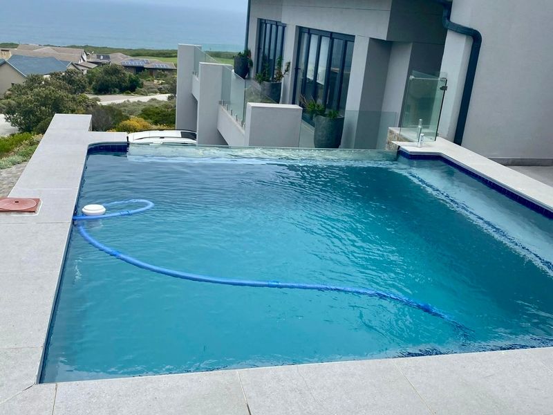An elevated infinity edge swimming pool featuring a glass balustrade and modern tiling, offering expansive coastal views.