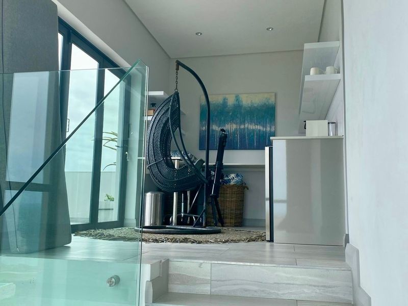 A modern, elevated living space featuring a glass balustrade, tiled staircase, and large sliding doors that provide ample natural light.