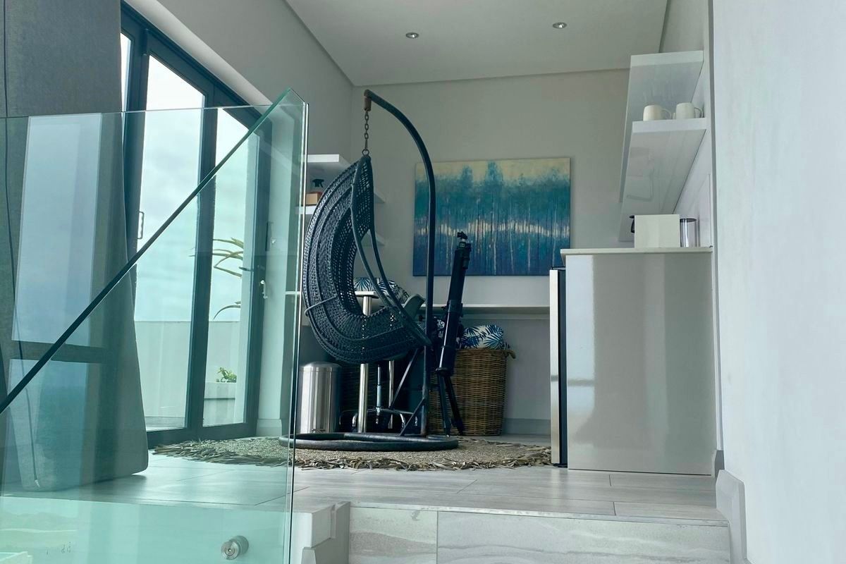 A modern, elevated living space featuring a glass balustrade, tiled staircase, and large sliding doors that provide ample natural light.