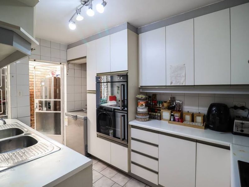 Functional kitchen featuring white cabinetry, built-in oven, double sink, and tiled backsplash, offering a practical layout with direct access to an exterior area.