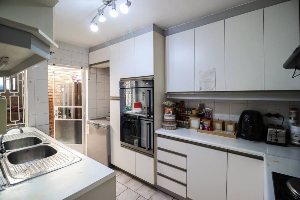Functional kitchen featuring white cabinetry, built-in oven, double sink, and tiled backsplash, offering a practical layout with direct access to an exterior area.