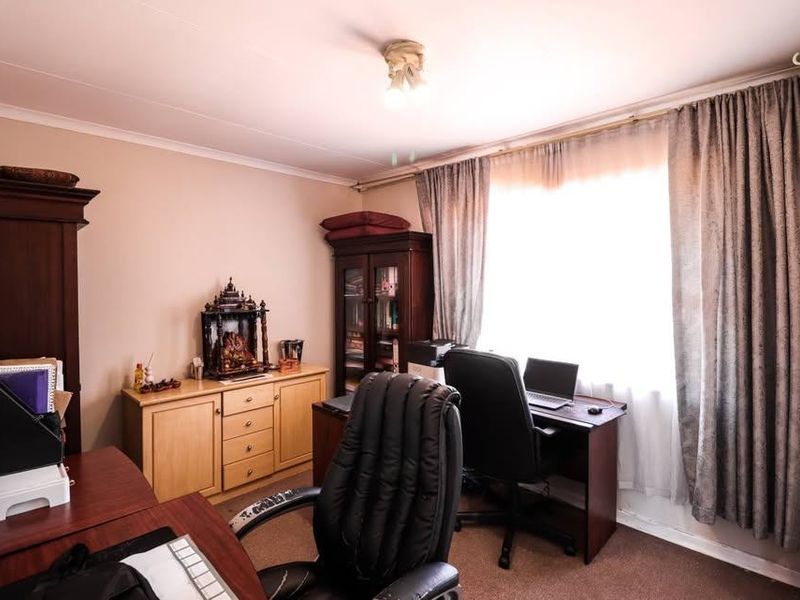 A functional bedroom or home office space featuring carpeted flooring and natural light through window curtains.