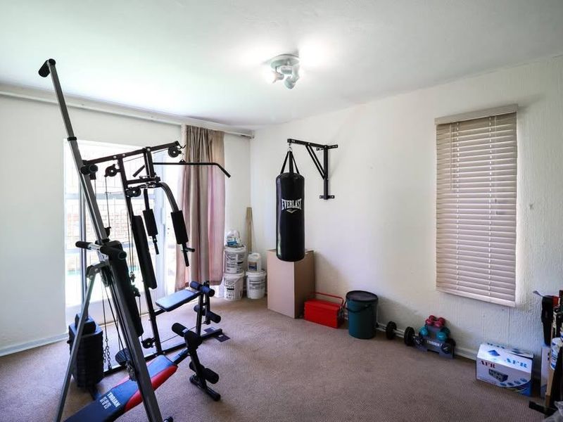 A bedroom currently utilized as a home gym, featuring neutral walls, carpeted flooring, and access to an outdoor area via a sliding glass door.