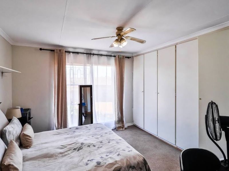 A bedroom featuring built-in cupboards, a ceiling fan, and a sliding door providing natural light.