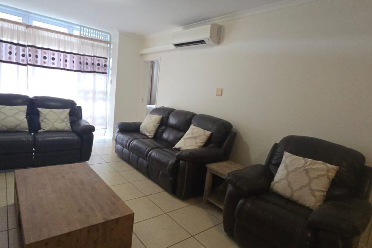 A spacious living room featuring tiled flooring, a wall-mounted air conditioning unit, and large windows providing natural light.