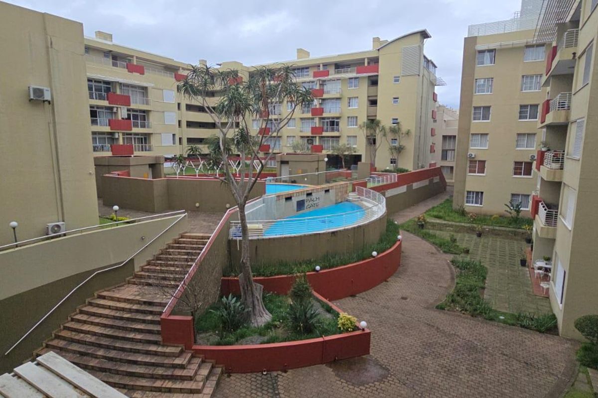View of the apartment complex courtyard featuring a swimming pool, paved walkways, landscaped garden beds, and communal staircases.
