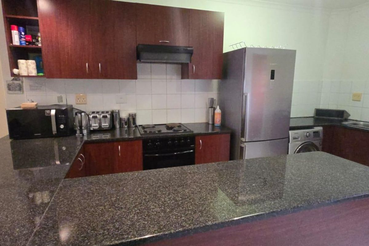 A functional kitchen featuring dark wood cabinetry, granite countertops, a built-in oven, hob, extractor fan, and a double sink.