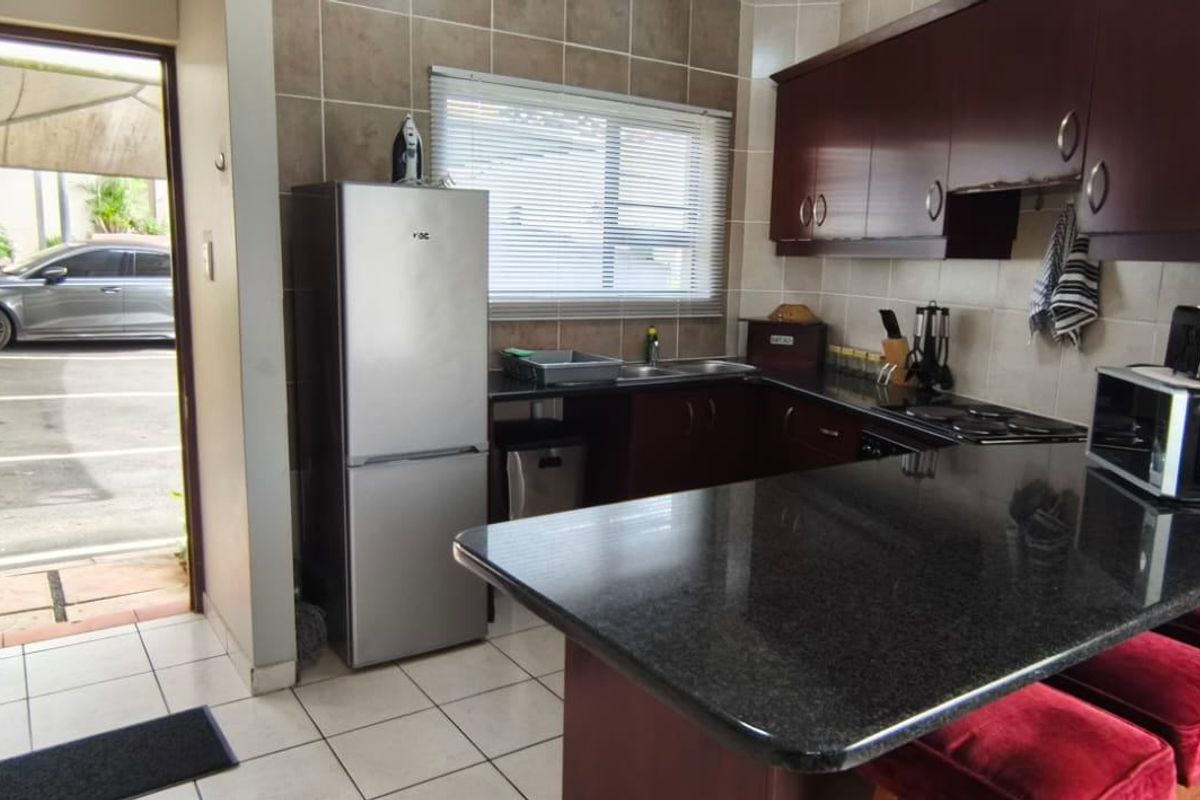 Functional kitchen featuring dark wood cabinetry, granite countertops, tiled backsplash, and a breakfast bar, with direct access to the exterior.