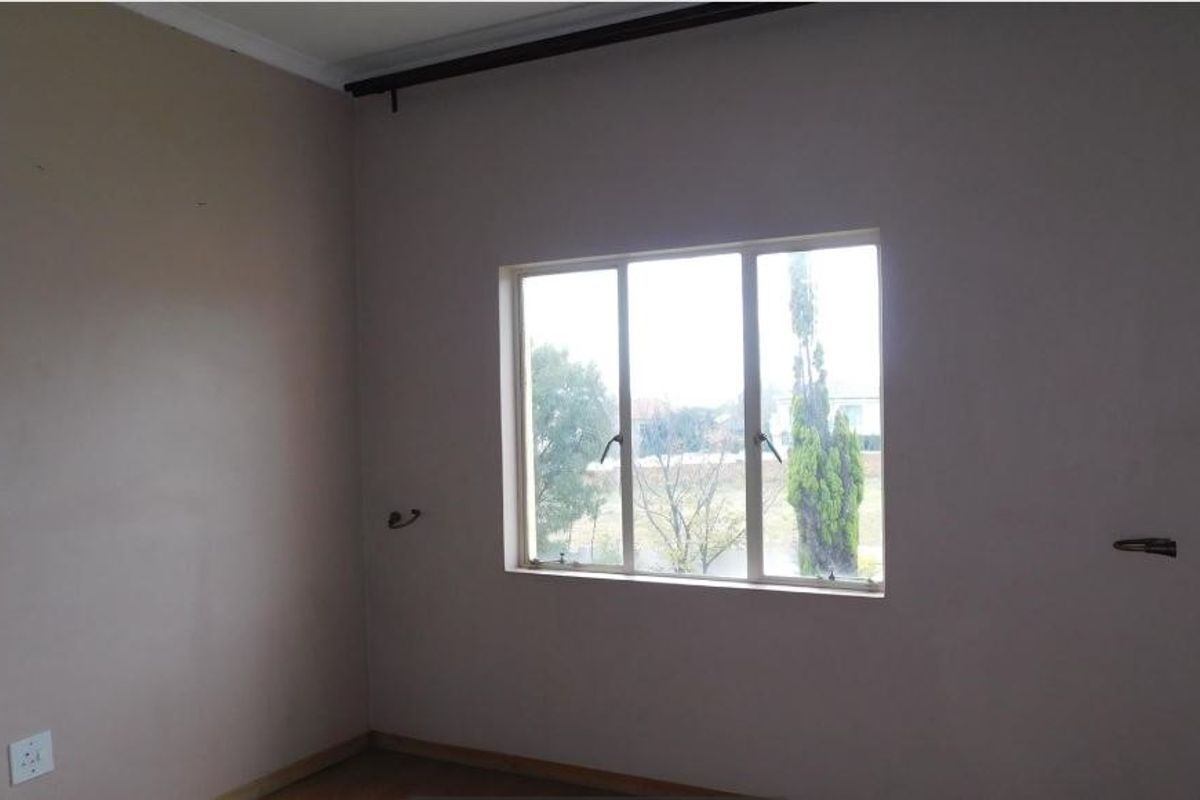 An empty bedroom featuring a metal-framed window, curtain rail, and basic electrical fixtures, requiring minor cosmetic updates to the walls and wiring.
