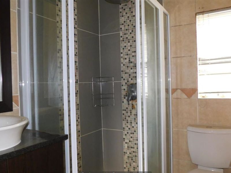 A functional bathroom featuring a shower enclosure, vanity basin with granite countertop, and a toilet, finished with neutral wall tiles and mosaic accents.