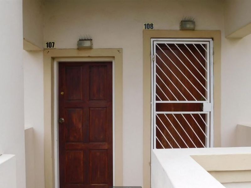 Exterior view of apartment unit entrances featuring a wooden door and a white security gate with unit number signage.