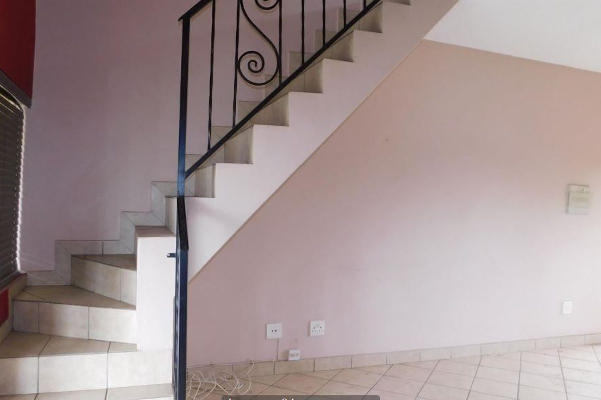 An open living area featuring a tiled staircase with a decorative wrought iron balustrade and neutral wall finishes.