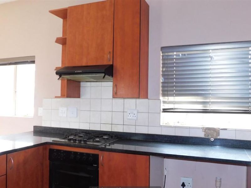 A functional kitchen featuring wooden cabinetry, a built-in oven with gas hob, extractor fan, and tiled backsplash, ready for a modern update.