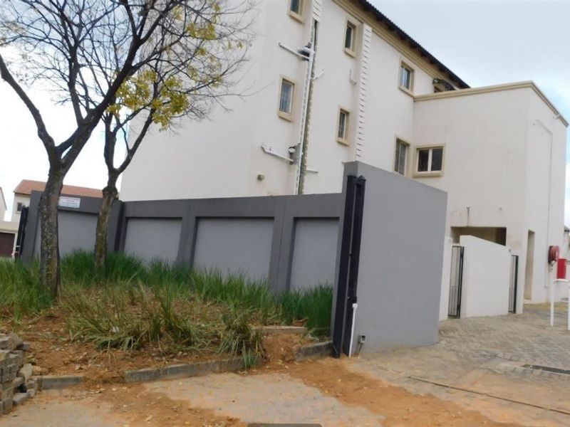 Exterior view of the apartment complex featuring a paved driveway, boundary wall, and multi-story building facade.