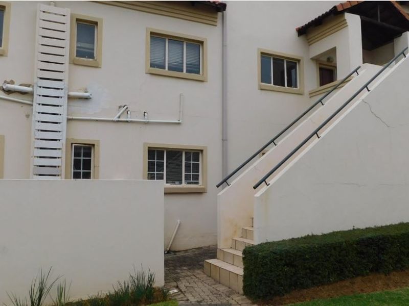 Rear exterior view of the apartment building featuring an external staircase, fire safety equipment, and paved access path.