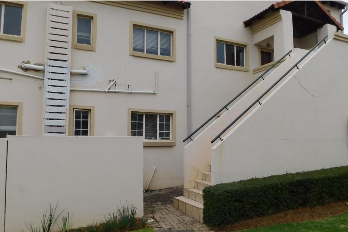 Rear exterior view of the apartment building featuring an external staircase, fire safety equipment, and paved access path.