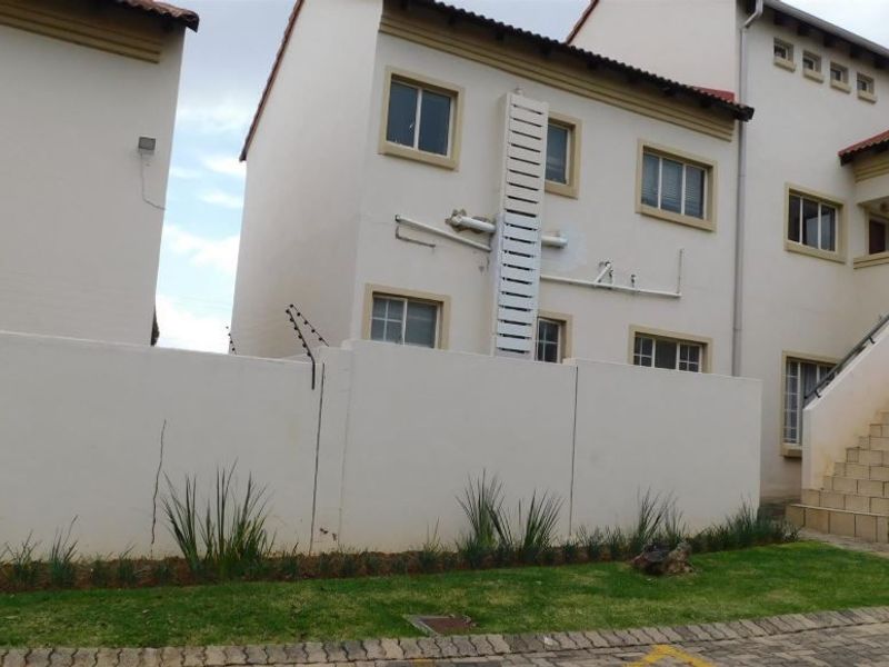 Exterior view of an apartment complex featuring a concrete boundary wall with electric fencing, paved driveway, and an external staircase.