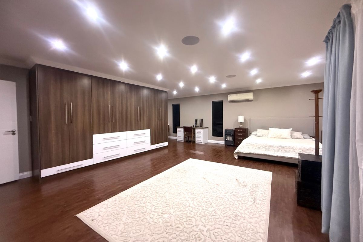 Spacious bedroom featuring extensive built-in cabinetry, recessed downlighting, split-system air conditioning, and polished hardwood flooring.