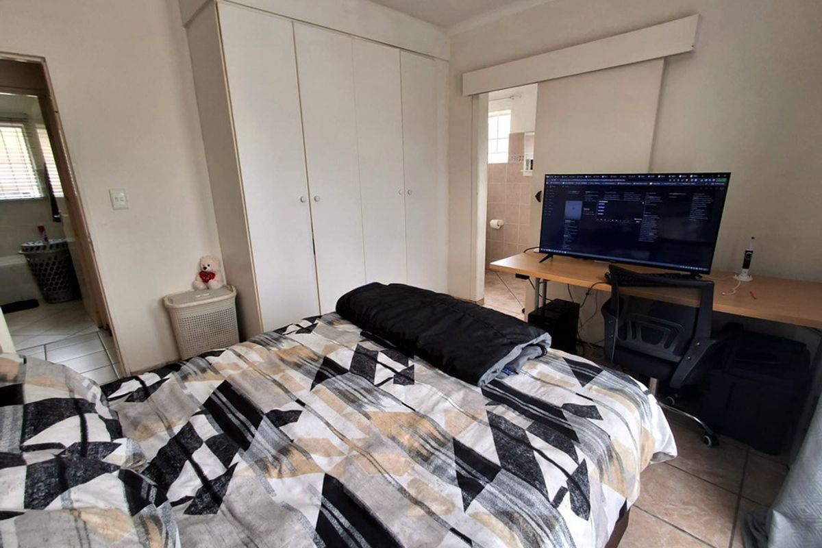 A functional bedroom featuring built-in wardrobes, tiled flooring, and an en-suite bathroom access point.
