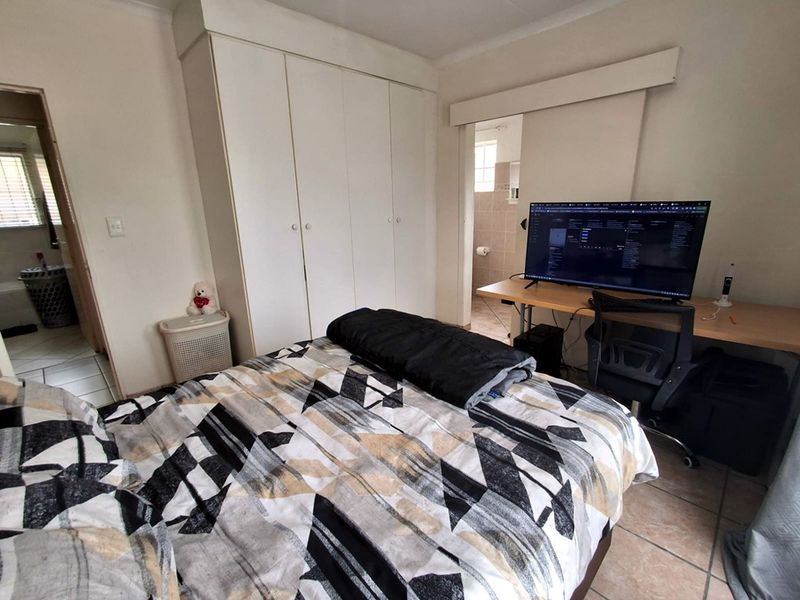 A functional bedroom featuring built-in wardrobes, tiled flooring, and an en-suite bathroom access point.