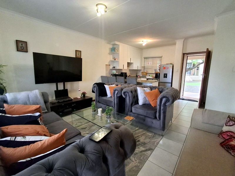 Open-plan living area featuring tiled flooring and a functional kitchen with built-in cabinetry and a breakfast counter, leading to an exterior entrance.