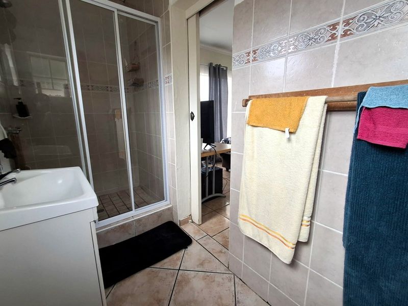 A functional bathroom featuring a tiled shower enclosure, vanity basin, and neutral wall tiling, providing a practical layout for daily use.