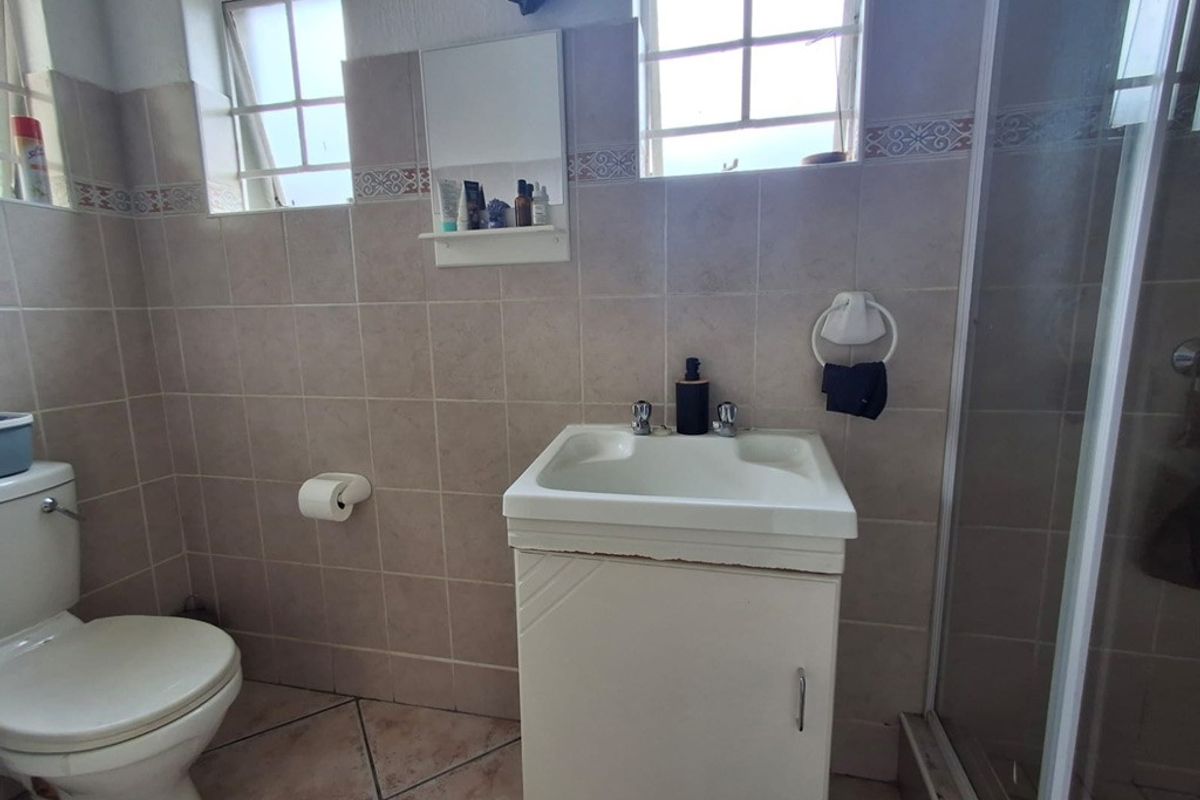 A functional bathroom featuring a vanity cabinet, toilet, and shower enclosure with neutral wall and floor tiling.
