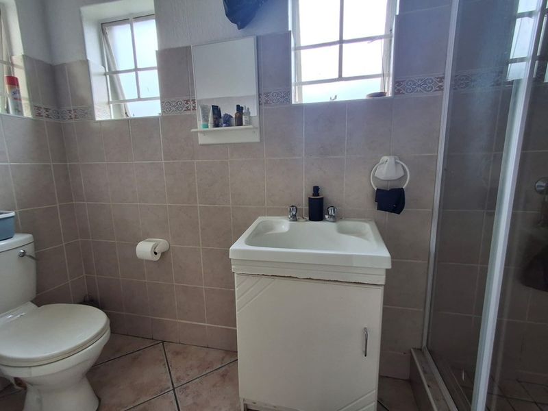A functional bathroom featuring a vanity cabinet, toilet, and shower enclosure with neutral wall and floor tiling.