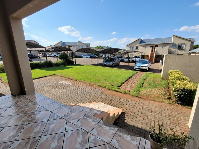 View of a communal residential courtyard featuring a paved patio, lawn area, and covered parking bays for residents.