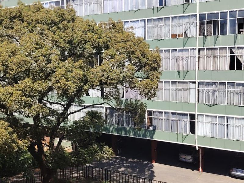 Exterior view of a multi-story apartment building featuring a green facade, large windows, and covered ground-level parking area.