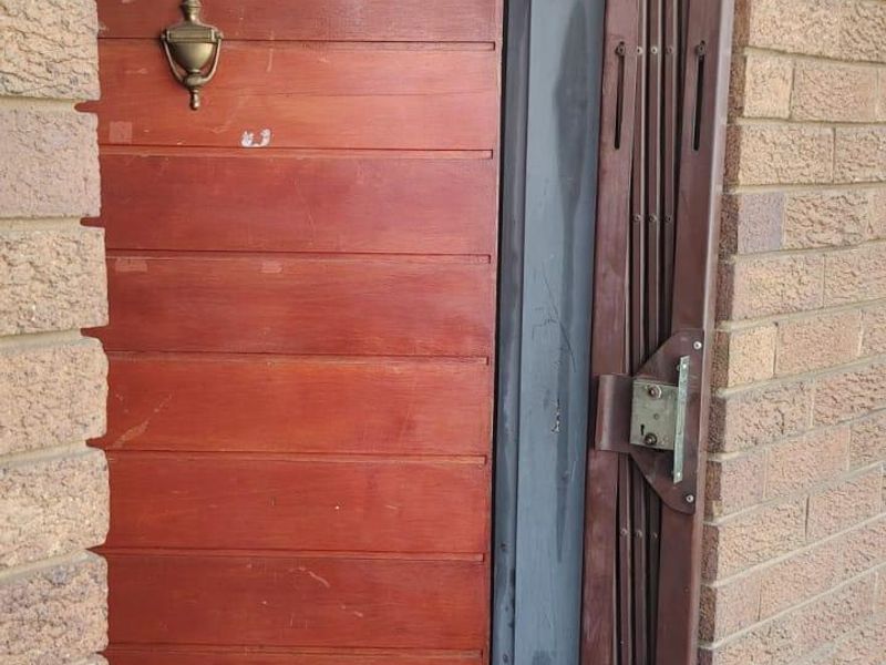 Entrance to apartment 404 featuring a timber front door with a brass knocker and a retractable security gate set within a brick facade.