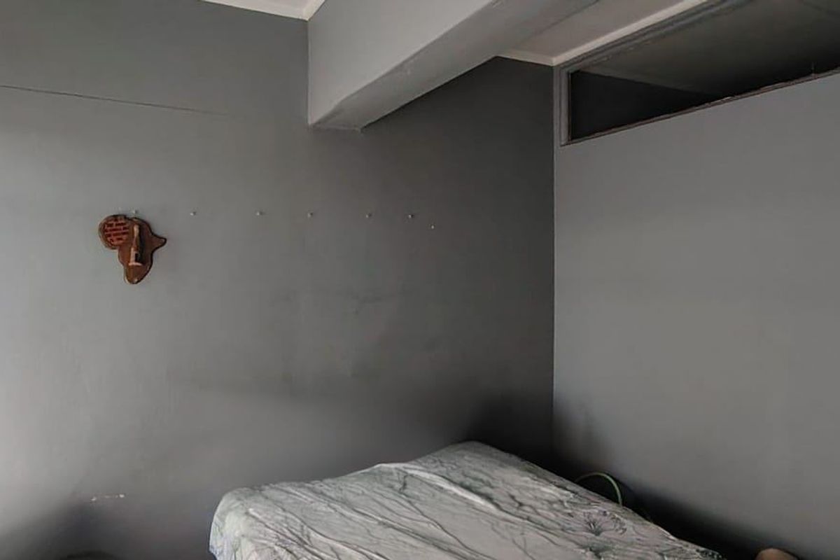 A bedroom featuring grey painted walls, a bulkhead, and a high-level transom window, requiring cosmetic updates to improve the overall finish.