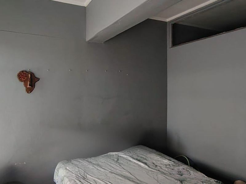 A bedroom featuring grey painted walls, a bulkhead, and a high-level transom window, requiring cosmetic updates to improve the overall finish.