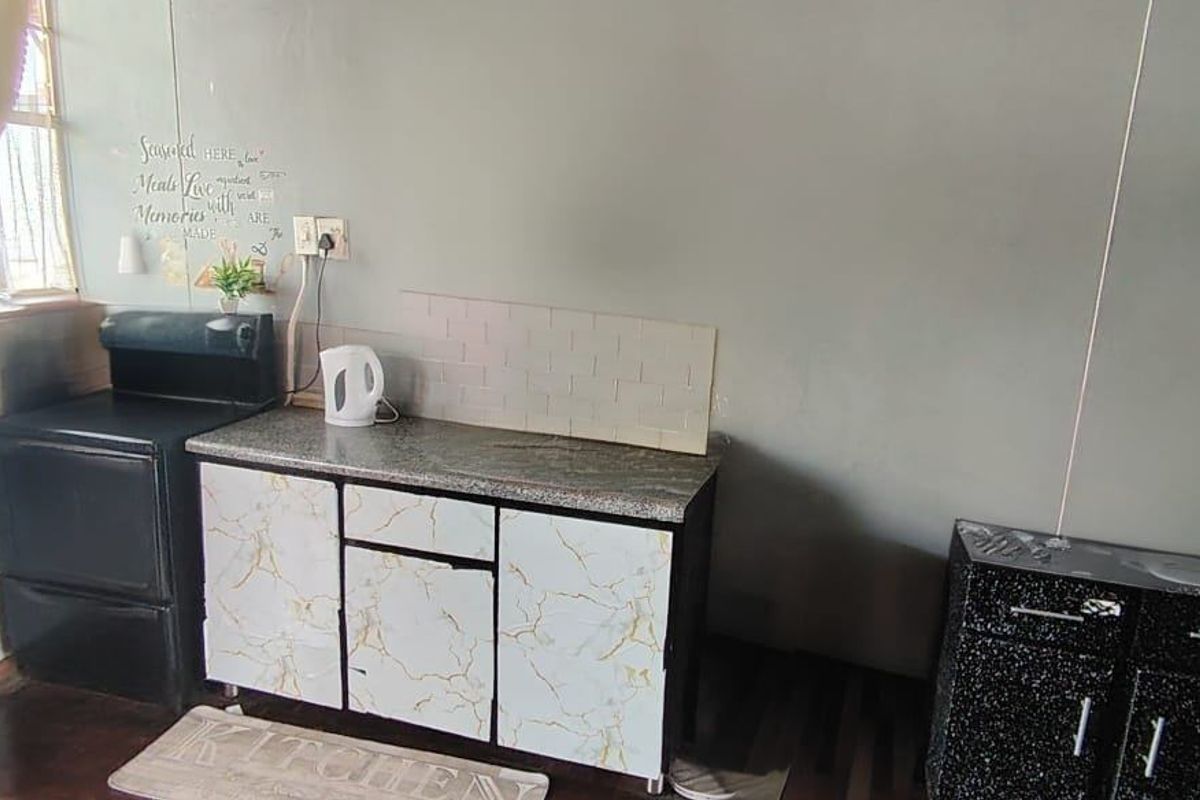A compact kitchen area featuring granite-look countertops, tiled backsplash, and built-in cabinetry, currently showing signs of wear and requiring cosmetic updates.