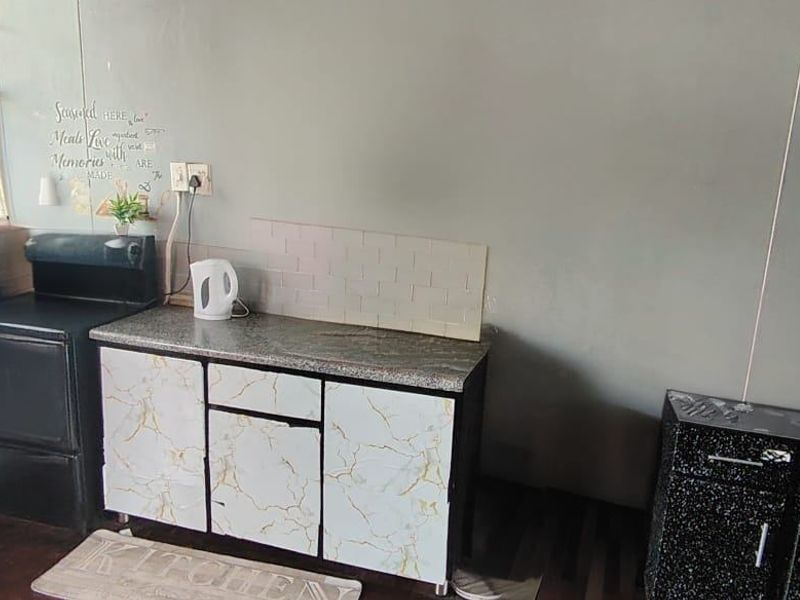 A compact kitchen area featuring granite-look countertops, tiled backsplash, and built-in cabinetry, currently showing signs of wear and requiring cosmetic updates.