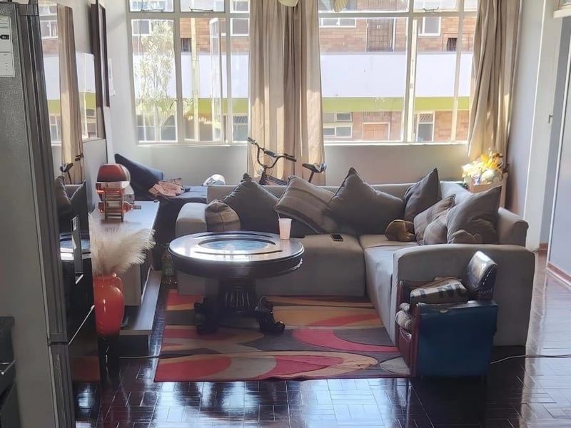 A living room featuring dark parquet flooring, a ceiling fan, and large windows that provide ample natural light.
