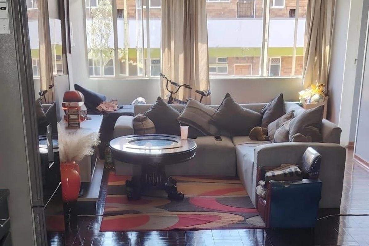 A living room featuring dark parquet flooring, a ceiling fan, and large windows that provide ample natural light.