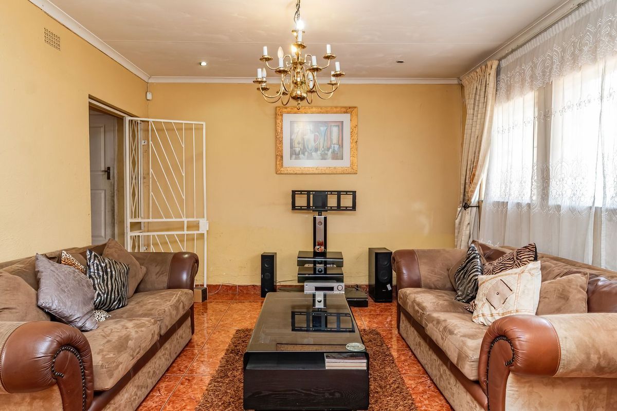 A living room featuring ceramic tile flooring, a central chandelier, and a security gate, with neutral wall finishes.