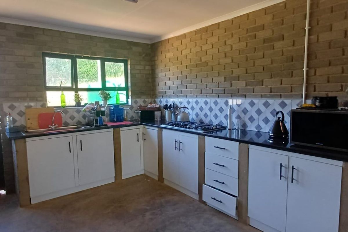 A functional kitchen featuring exposed brick walls, white cabinetry, granite countertops, a gas hob, and a tiled backsplash with a double sink.
