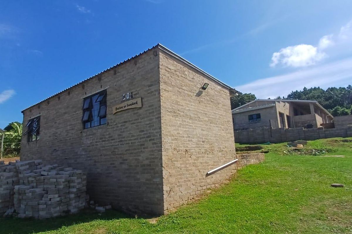 Rear view of a face brick house under construction, featuring steel windows and a metal roof, set on a large grassed plot.