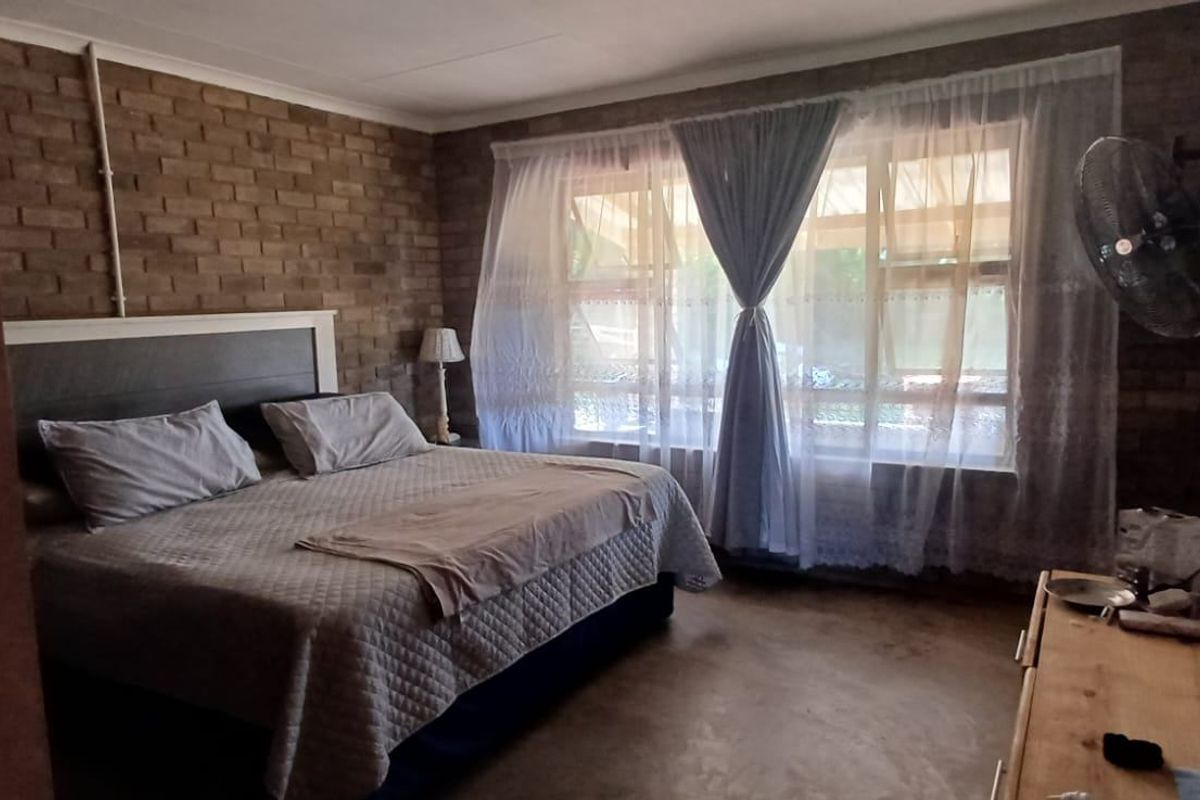 A bedroom featuring exposed brick walls, concrete flooring, and a large window allowing natural light into the space.
