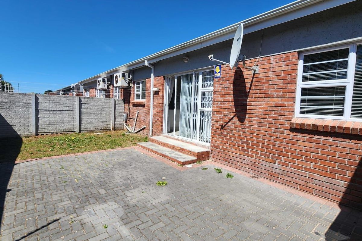 Rear exterior view of the cluster home featuring a brick facade, paved patio area, sliding door access, and perimeter boundary wall.