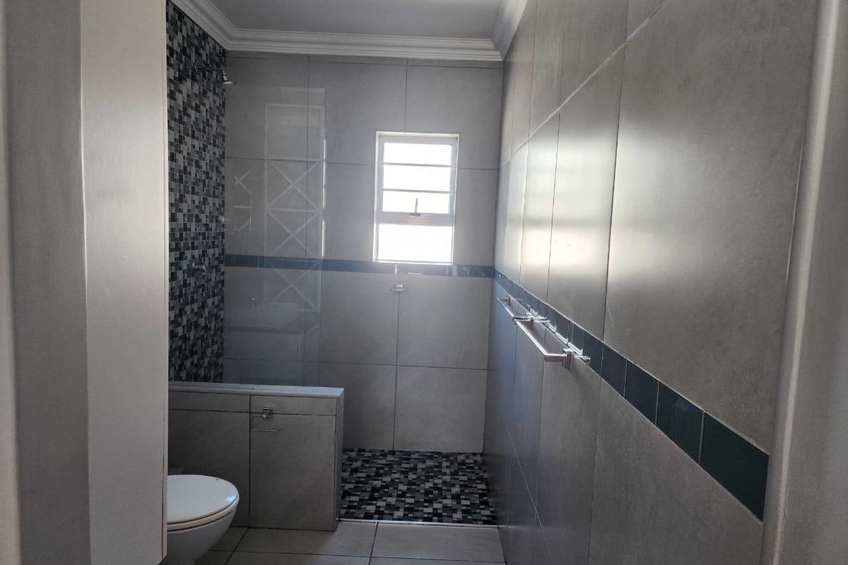A modern bathroom featuring a walk-in shower with mosaic tile accents, large format wall tiles, and a built-in vanity unit.