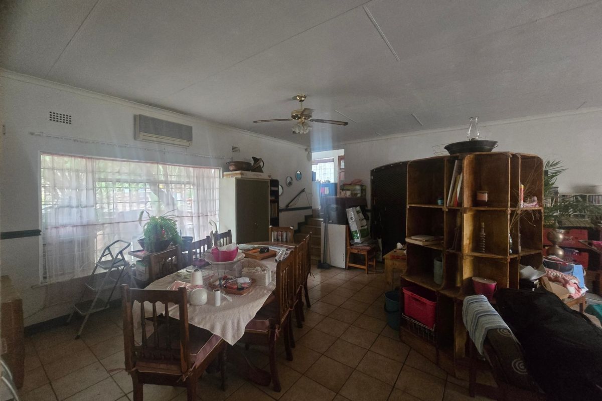 A spacious living and dining area featuring tiled flooring, a ceiling fan, and a wall-mounted air conditioning unit.
