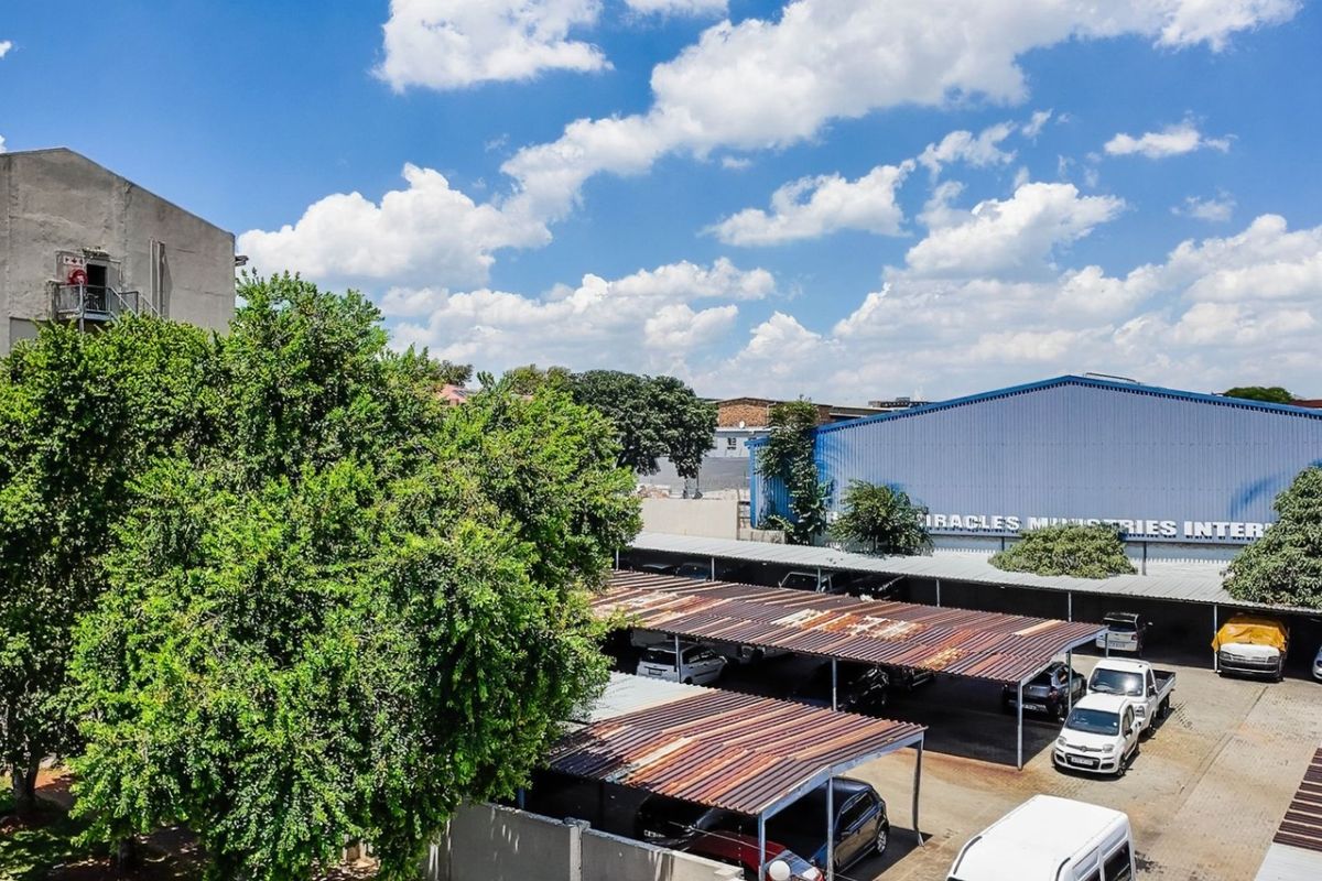 Exterior view of the commercial property featuring a large warehouse building and multiple corrugated metal carport structures in the parking area.