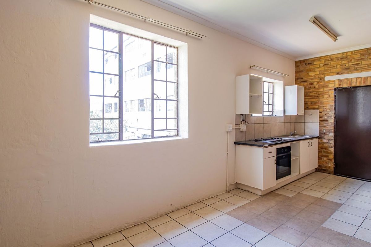 A functional, empty kitchen featuring built-in cabinetry, an integrated oven and hob, tiled flooring, and an exposed brick feature wall.
