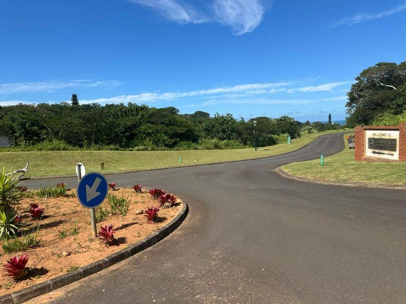 A view of the entrance road and landscaped verge leading into the Ukusa estate, featuring paved surfaces and established greenery.