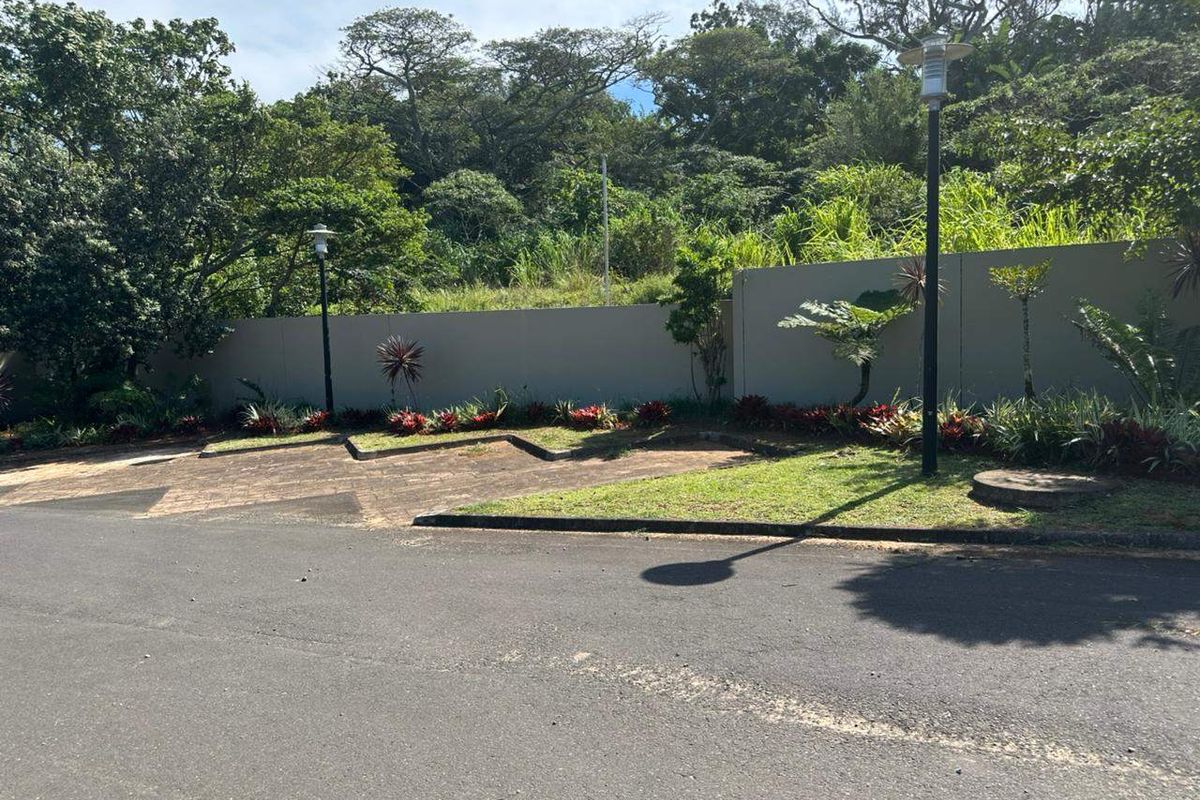 A well-maintained residential plot featuring a paved driveway, boundary wall, and established garden landscaping with integrated lighting.